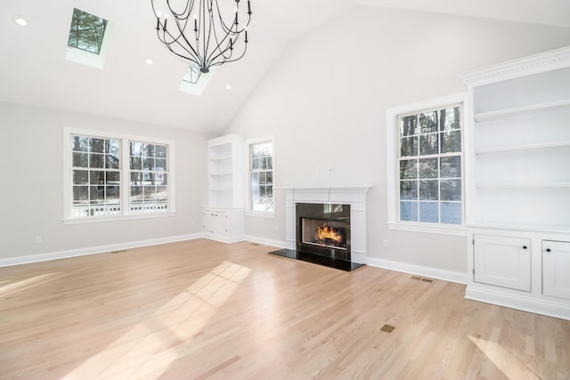 unfurnished living room with an inviting chandelier, light wood-type flooring, a premium fireplace, and lofted ceiling with skylight