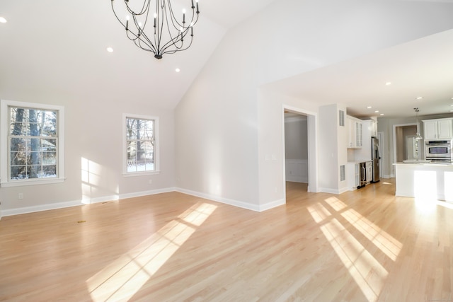 unfurnished living room featuring a wealth of natural light, an inviting chandelier, and light wood-type flooring