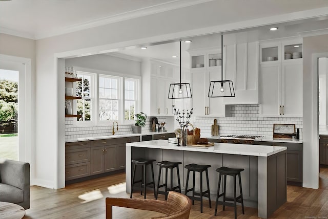 kitchen with wood-type flooring, a kitchen breakfast bar, decorative light fixtures, white cabinets, and a center island