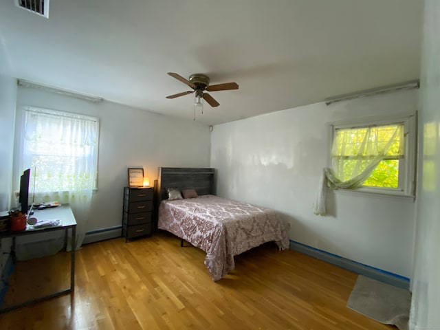 bedroom with light hardwood / wood-style flooring, a baseboard heating unit, multiple windows, and ceiling fan