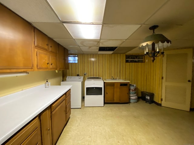 kitchen with a drop ceiling, wooden walls, washer and clothes dryer, and sink