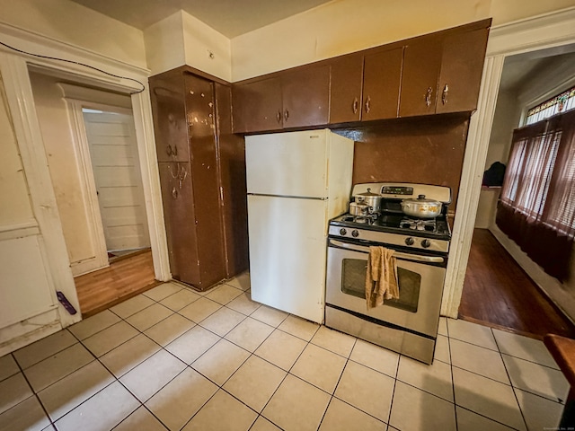 kitchen with stainless steel gas range, light hardwood / wood-style floors, dark brown cabinetry, and white fridge