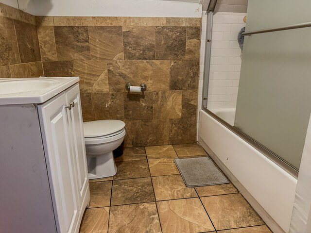 full bathroom featuring tile walls, vanity, toilet, and bath / shower combo with glass door