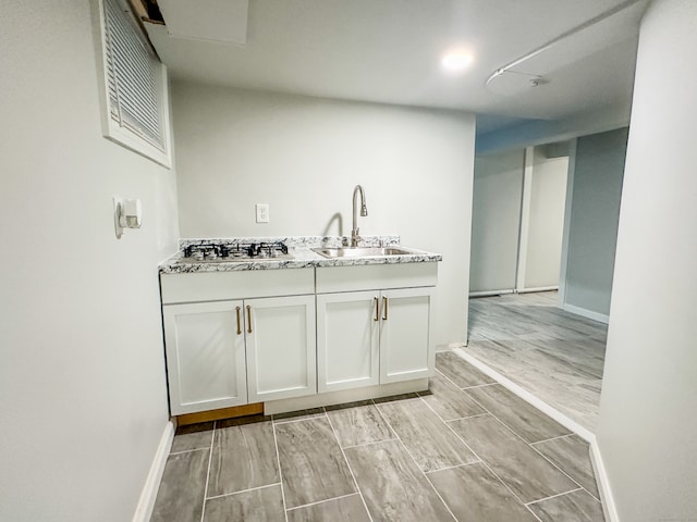 interior space with sink, white cabinetry, stainless steel gas stovetop, light stone countertops, and light hardwood / wood-style floors