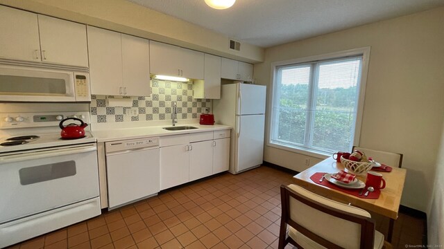 kitchen with dark tile patterned flooring, white cabinets, backsplash, white appliances, and sink