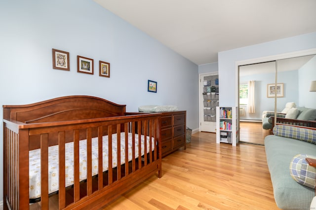 bedroom with light hardwood / wood-style flooring, a baseboard radiator, a closet, and a crib