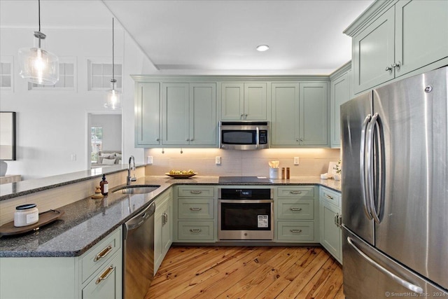 kitchen with pendant lighting, sink, green cabinetry, dark stone countertops, and stainless steel appliances