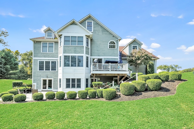 rear view of property featuring a deck, a lawn, and a patio area