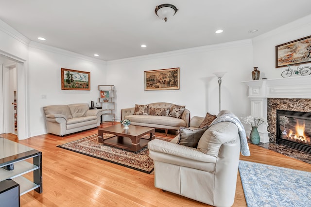 living room with light wood-type flooring, ornamental molding, and a high end fireplace