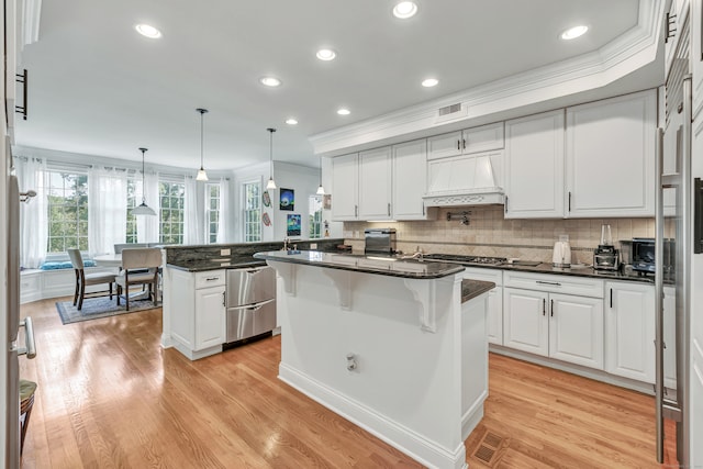 kitchen with kitchen peninsula, custom range hood, light hardwood / wood-style flooring, stainless steel appliances, and crown molding