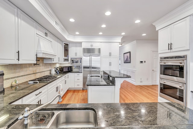 kitchen featuring white cabinetry, built in appliances, light wood-type flooring, crown molding, and custom exhaust hood