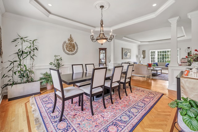 dining room featuring light wood-type flooring, a tray ceiling, a notable chandelier, ornamental molding, and ornate columns