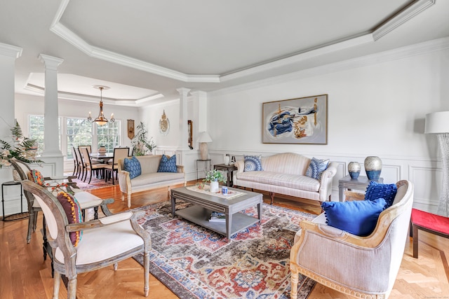 living room featuring crown molding, decorative columns, a tray ceiling, and an inviting chandelier