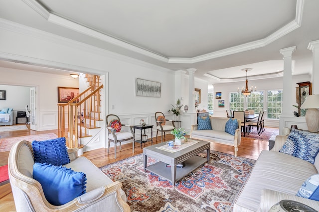 living room featuring light wood-type flooring, a chandelier, decorative columns, a raised ceiling, and ornamental molding