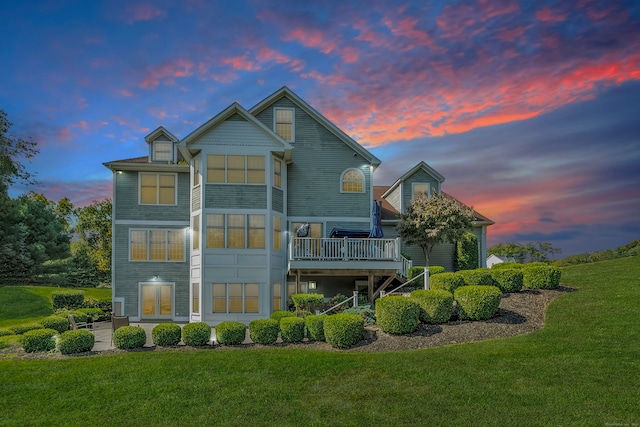 back house at dusk featuring a lawn and a wooden deck