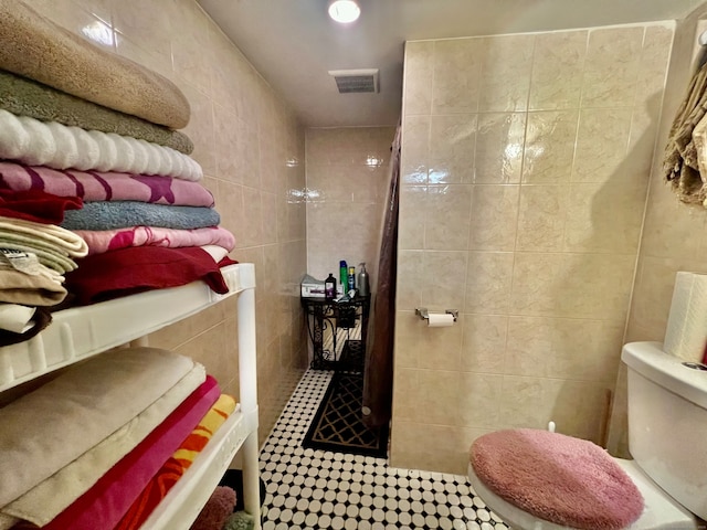 bathroom with tile walls, tiled shower, and toilet