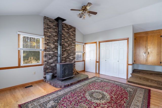 living room with ceiling fan, a wood stove, vaulted ceiling, and light wood-type flooring