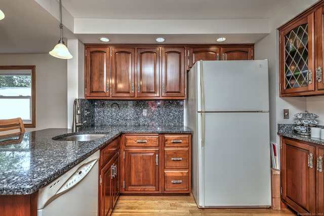 kitchen featuring dark stone counters, light hardwood / wood-style floors, sink, hanging light fixtures, and white appliances