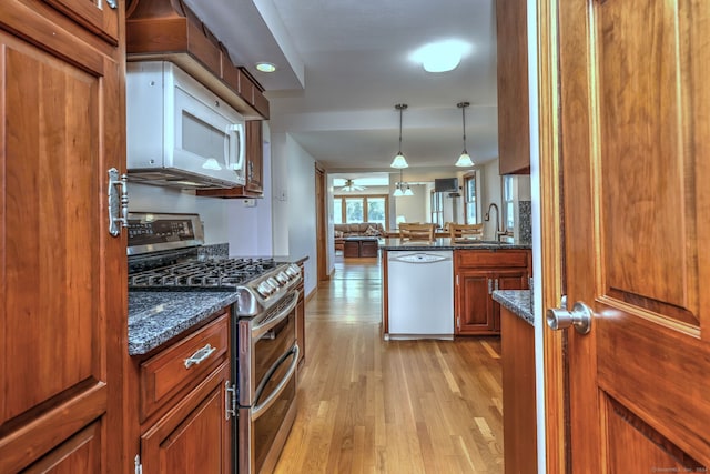 kitchen with pendant lighting, sink, white appliances, light hardwood / wood-style flooring, and dark stone countertops