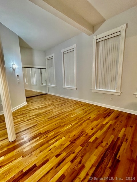 empty room featuring vaulted ceiling with beams and light wood-type flooring