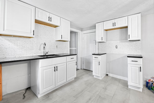 kitchen with a textured ceiling, backsplash, white cabinetry, and sink