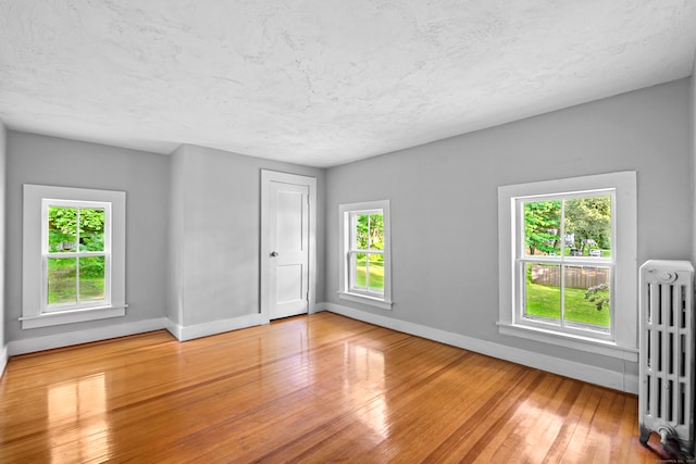 empty room featuring radiator heating unit, a textured ceiling, and hardwood / wood-style flooring