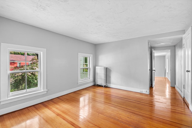 unfurnished room with radiator heating unit, a textured ceiling, and light hardwood / wood-style flooring