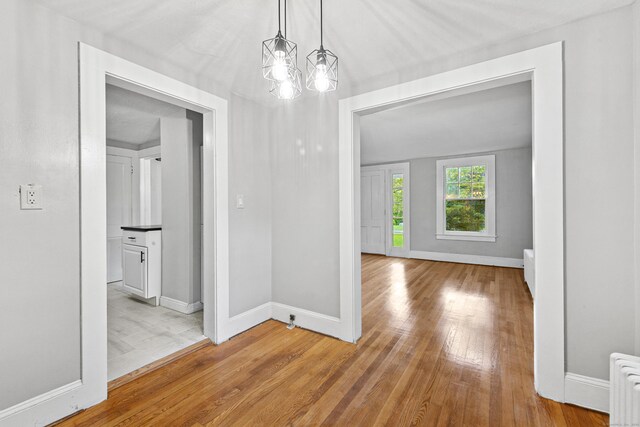 hall featuring light hardwood / wood-style flooring, a chandelier, and radiator heating unit