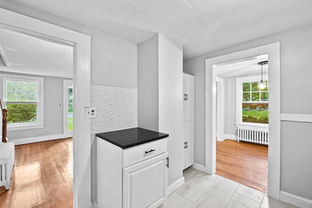 kitchen with radiator heating unit, brick wall, a textured ceiling, white cabinetry, and light hardwood / wood-style floors