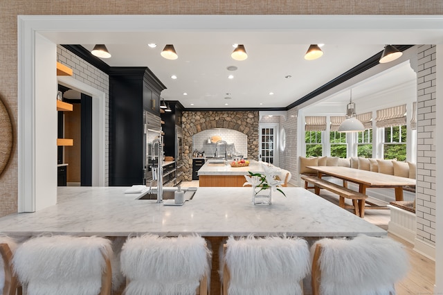 kitchen with sink, brick wall, decorative light fixtures, light wood-type flooring, and crown molding