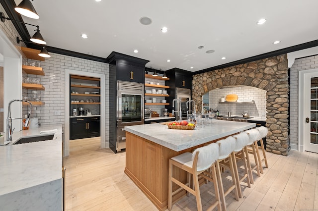 kitchen with light hardwood / wood-style floors, built in refrigerator, light stone countertops, ornamental molding, and sink