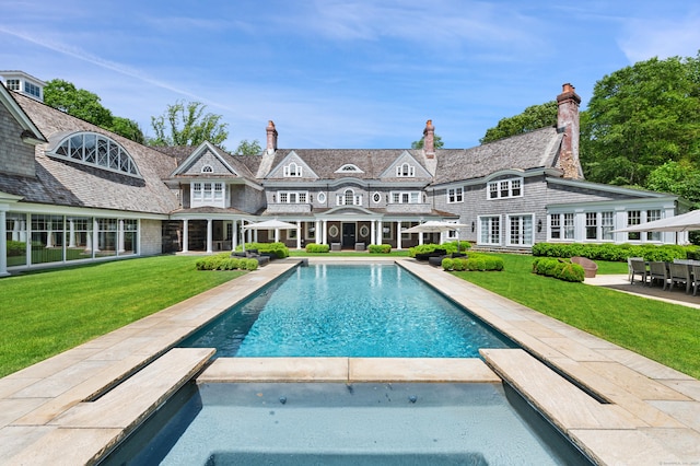 9 Cowdray Park Dr, Greenwich, CT 06831 - back of property with a patio, a pool with connected hot tub, a chimney, and a lawn