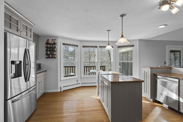 kitchen featuring appliances with stainless steel finishes, decorative light fixtures, a baseboard radiator, gray cabinetry, and dark stone counters