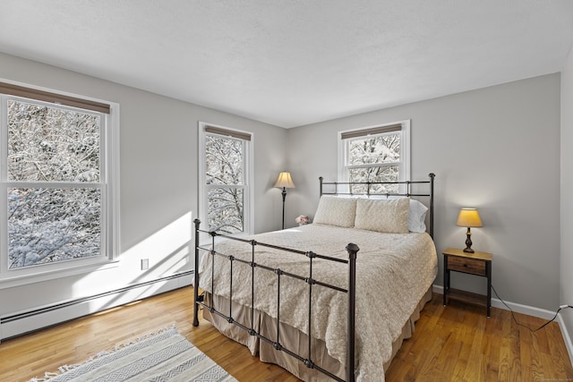 bedroom with multiple windows, wood-type flooring, and baseboard heating