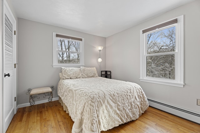 bedroom with baseboard heating, hardwood / wood-style floors, and a closet