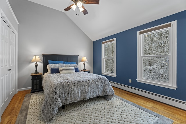 bedroom with a baseboard radiator, lofted ceiling, hardwood / wood-style floors, and a closet