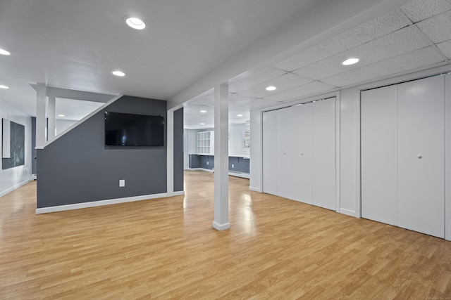 unfurnished living room with baseboard heating, a paneled ceiling, and light wood-type flooring