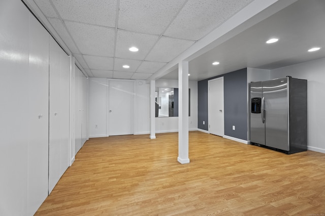 basement featuring a paneled ceiling, stainless steel fridge, and light wood-type flooring