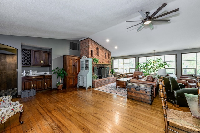 living room with light hardwood / wood-style flooring, a wealth of natural light, vaulted ceiling, and a fireplace