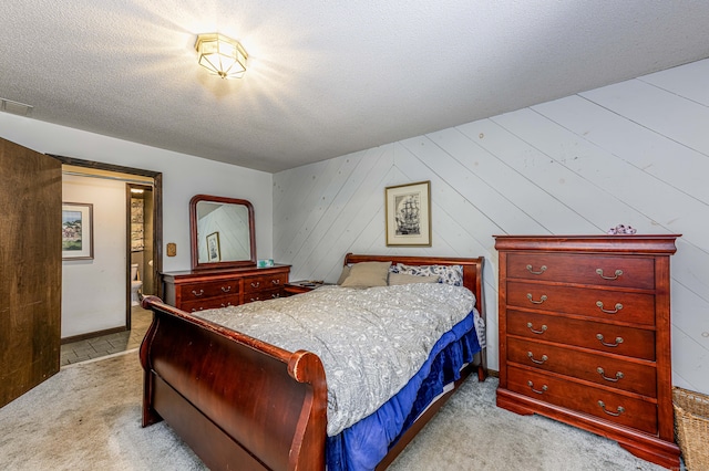 bedroom featuring a textured ceiling, wood walls, and light colored carpet