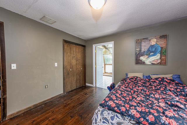 bedroom with a textured ceiling, dark wood-type flooring, and a closet