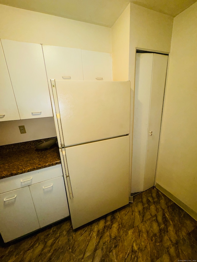 kitchen with dark stone counters, white cabinetry, and white refrigerator