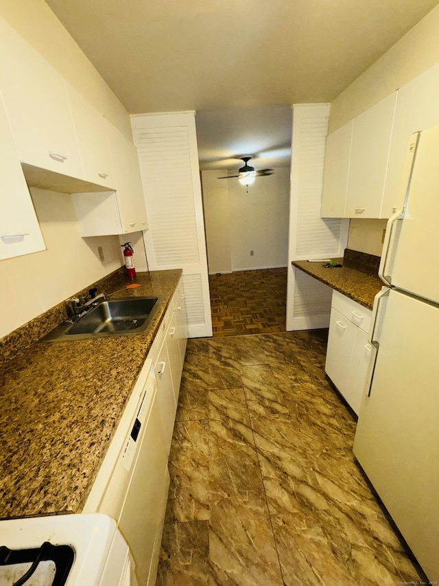 kitchen with dark countertops, a sink, white appliances, stone finish flooring, and white cabinetry