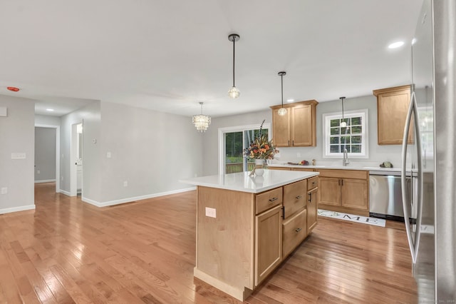 kitchen with a notable chandelier, a kitchen island, appliances with stainless steel finishes, and light hardwood / wood-style flooring