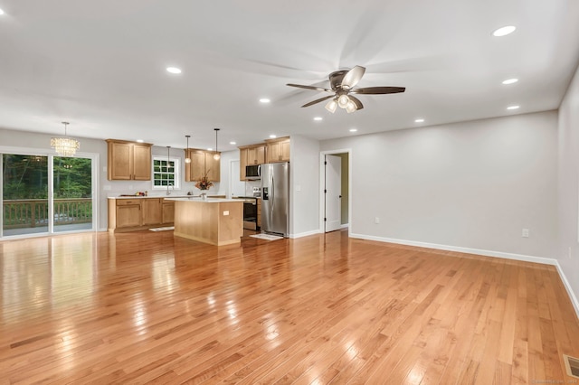 unfurnished living room with light wood-type flooring and ceiling fan with notable chandelier