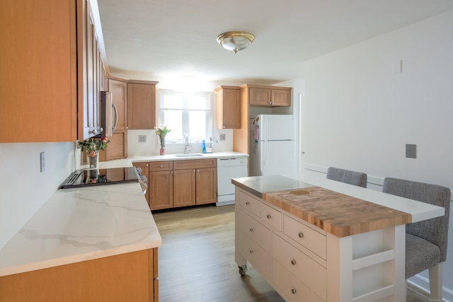 kitchen with sink, light stone countertops, white appliances, a center island, and light wood-type flooring