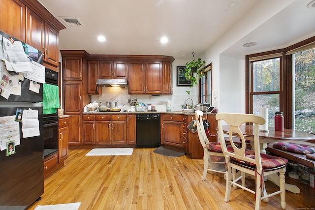 kitchen featuring light stone countertops, light hardwood / wood-style floors, black appliances, and decorative backsplash