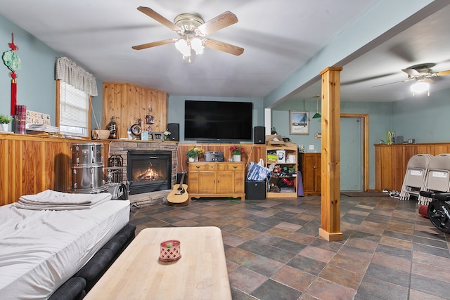 living room with a stone fireplace, wooden walls, and ceiling fan