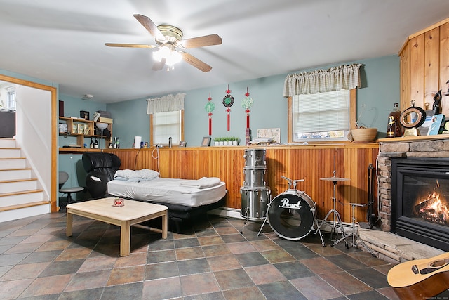 interior space featuring ceiling fan, a stone fireplace, baseboard heating, and wood walls