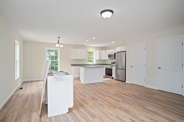 kitchen featuring white cabinetry, appliances with stainless steel finishes, decorative light fixtures, light hardwood / wood-style floors, and a center island